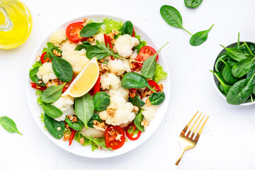 Useful vegan cauliflower salad with baked paprika, cherry tomatoes, spinach with walnuts, white table background, top view