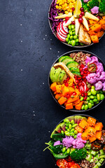Vegan buddha bowls assortment with pumpkin, quinoa, tomatoes, spinach, avocado, radish, soybeans edamame, tofu, cabbage and seeds, black table background, top view. Autumn or winter healthy food