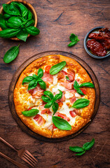 Homemade pizza with pancetta, mozzarella cheese, spicy sauce and green basil leaves on old wooden table background, top view