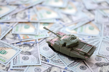 Toy tank on US hundred dollar bills banknotes close up. The concept of war costs, military spending...