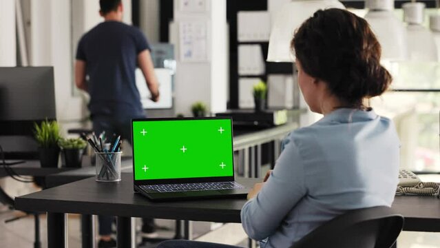 Employee checks greenscreen on laptop, looking at isolated copyspace mockup screen in coworking space. Young woman reviewing pc display layout with blank chromakey template. Handheld shot.