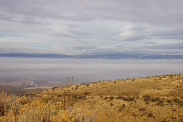 An oblique panorama with dry grass in the foreground, a landscape with roads, fields, meadows, mountains that are hidden in clouds and fog on the horizon. Picturesque landscape with beautiful sky