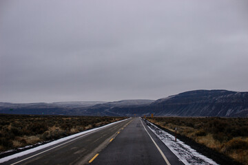 Asphalt road in the middle of high mountains, covered with fog and clouds, at dusk. American winter landscape of a mountainous area covered with fir forest