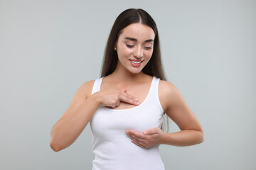 Beautiful young woman doing breast self-examination on light grey background