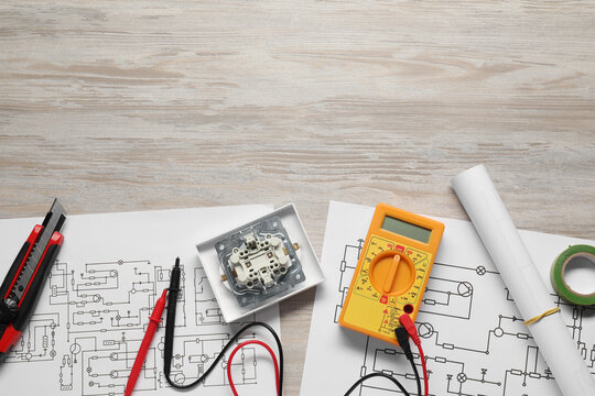 Wiring diagrams and digital multimeter on white wooden table, flat lay. Space for text