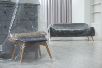 Grey chest of drawers, stool and sofa covered with plastic film at home