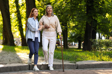 Senior lady with walking cane and young woman in park. Space for text