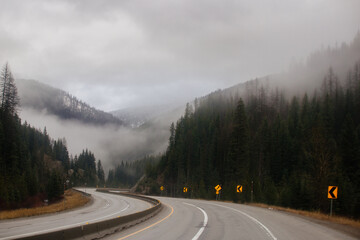 Asphalt road in the middle of high mountains, covered with fog and clouds, at dusk. American winter...
