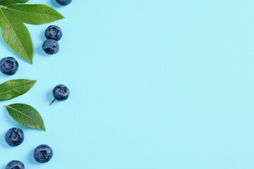 Tasty fresh blueberries with green leaves on light blue background, flat lay. Space for text