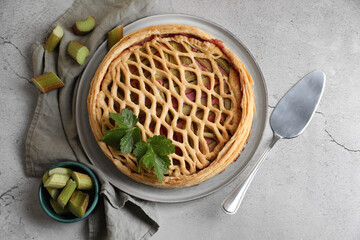 Freshly baked rhubarb pie, cut stalks and cake server on light grey table, flat lay