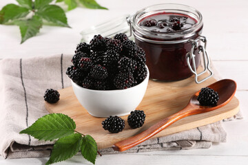 Fresh ripe blackberries, tasty jam and leaves on white wooden table