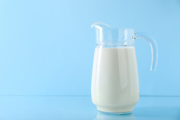 Jug of fresh milk on light blue background, space for text