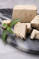 Pieces of tasty halva and mint served on light grey table, closeup