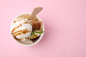 Tasty ice cream with caramel sauce, mint and candy in paper cup on pink background, top view. Space for text