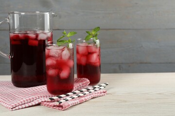 Delicious iced hibiscus tea with mint and straws on white wooden table, space for text