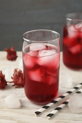 Delicious hibiscus tea with ice cubes and straws on white wooden table, closeup