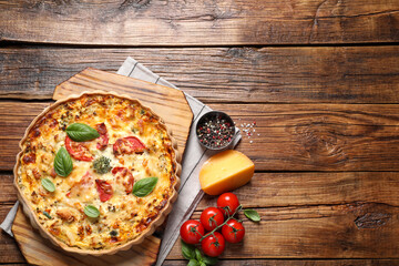 Tasty quiche with tomatoes, basil and cheese served on wooden table, flat lay. Space for text