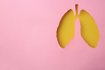Pink paper with hole in shape of human lungs, top view. Space for text