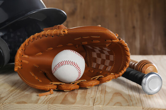 Baseball glove, bats, ball and batting helmet on wooden table