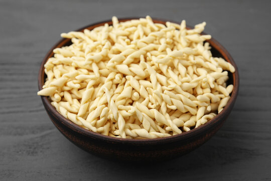Uncooked trofie pasta in bowl on grey wooden table, closeup