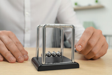 Man playing with Newton's cradle at wooden table, closeup. Physics law of energy conservation