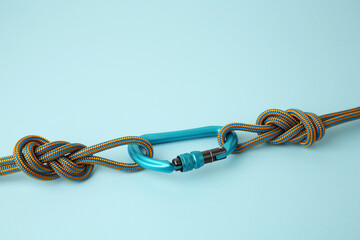 One metal carabiner with ropes on light blue background, space for text