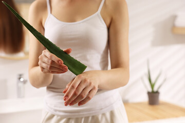 Young woman applying aloe gel from leaf onto her hand in bathroom, closeup