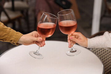 Women clinking glasses with rose wine at white table in outdoor cafe, closeup