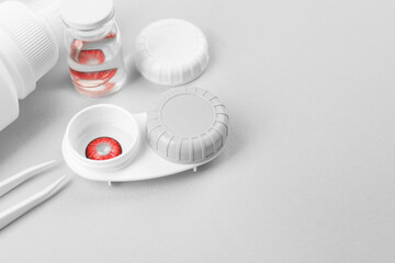 Case with red contact lenses, bottle of solution and tweezers on light grey background. Space for...