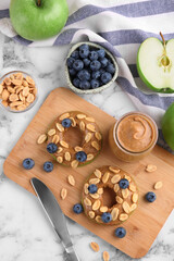 Fresh green apples with peanut butter, blueberries and nuts on white marble table, flat lay