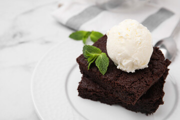 Tasty brownies served with ice cream and mint on white marble table, closeup. Space for text