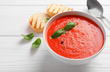 Delicious tomato cream soup in bowl on white wooden table, space for text