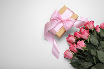 Gift box wrapped with pink bow and beautiful flowers on white background, flat lay. Space for text