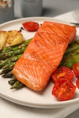 Tasty grilled salmon with asparagus, tomatoes and lemon on table, closeup