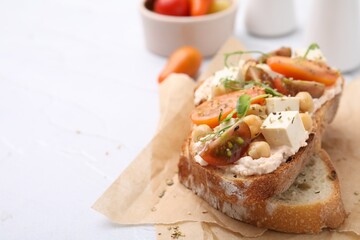 Tasty vegan sandwich with tomatoes, tofu and chickpeas on white textured table, closeup. Space for text