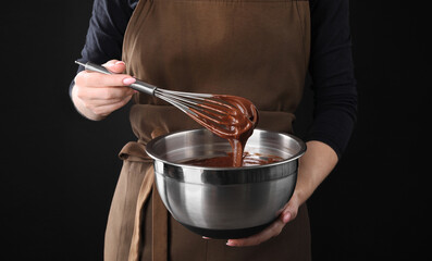 Woman with whisk mixing chocolate cream on black background, closeup