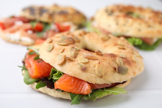 Tasty bagel with salmon and salad mix on white tiled table, closeup