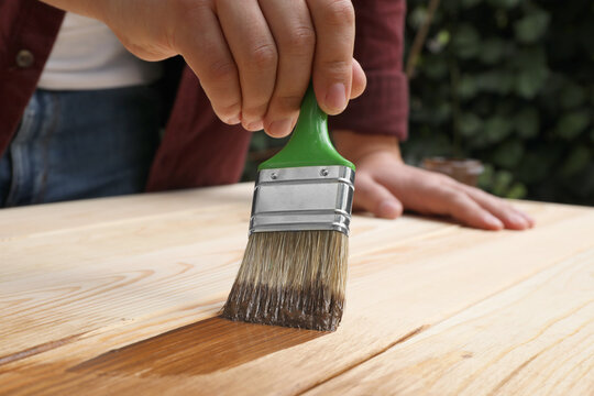 Man applying wood stain onto wooden surface against blurred background, closeup