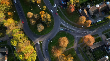 Autumn Aerial View,An aerial shot reveals a vibrant autumn tapestry of gold, red, and green trees, with a winding road leading to a roundabout. A stunning perspective on nature's seasonal transformati