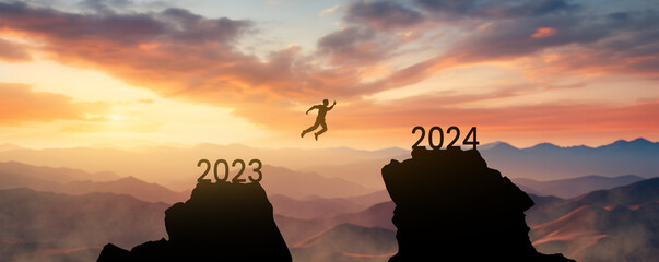 silhouette of a man jumping from one mountain to another leaving the year 2023 behind and reaching the new year 2024 - concept of setting goals for the next year