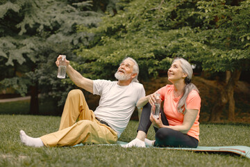 Senior couple sitting on exercise mats at park and talking