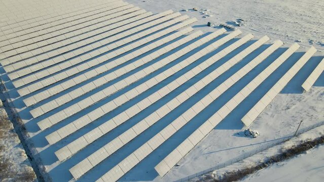 Aerial view of snow covered sustainable electric power plant with many rows of solar photovoltaic panels for producing clean electrical energy. Low effectivity of renewable electricity in winter