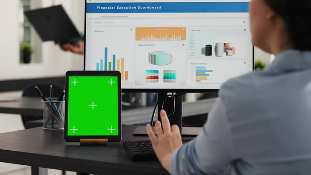Specialist works with greenscreen tablet in open floor plan office, presenting isolated display on modern device. Businesswoman using pc monitor and blank chromakey layout on mini screen.