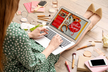 Woman with laptop, makeup products and accessories shopping online on light wooden floor, closeup