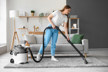 Young woman vacuuming carpet at home - obrazy, fototapety, plakaty