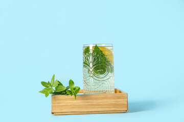 Wooden mini drawer with glass of fresh icy mint tea and lemon on blue background