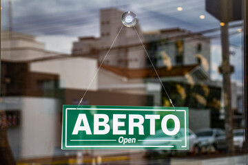 Bilingual sign with the words Aberto and Open in Portuguese and English on the glass door of a store in Brazil - obrazy, fototapety, plakaty