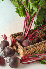 Wicker basket of fresh beets with green leaves on light background