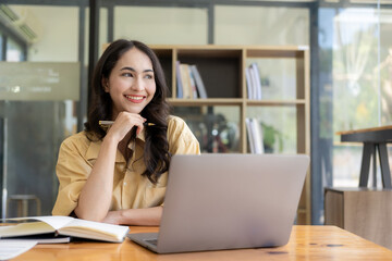 Ambitious Asian girl working from home Looking at laptop screen and financial documents, woman is checking email or doing research while working remotely.