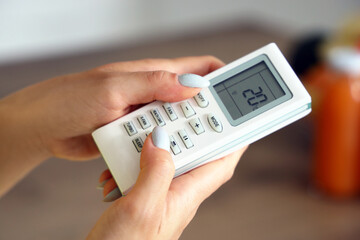 Young woman with air conditioner remote control in kitchen, closeup